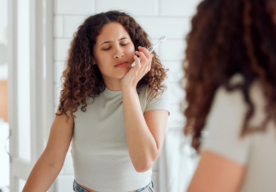Toothache, oral pain and dental sensitivity for a woman brushing her teeth in the morning. African American female suffering with a painful, hurting or inflammation in her mouth in the bathroom