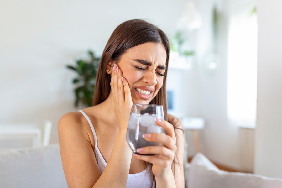 Young woman with sensitive teeth and hand holding glass of cold water with ice. Healthcare concept. woman drinking cold drink, glass full of ice cubes and feels toothache, pain